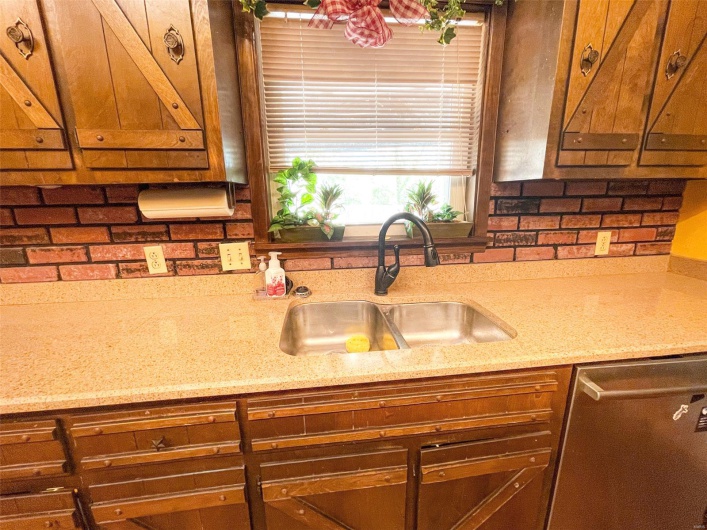Kitchen with brown cabinetry, light stone counters, stainless steel dishwasher, and a sink