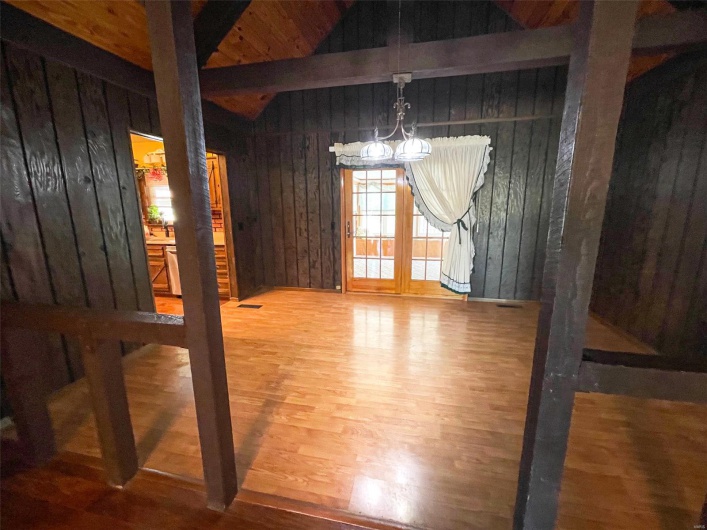 Unfurnished dining area with visible vents, a chandelier, wood finished floors, wood walls, and vaulted ceiling with beams