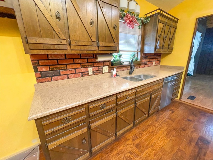 Kitchen featuring baseboards, a sink, dark wood finished floors, brown cabinets, and stainless steel dishwasher