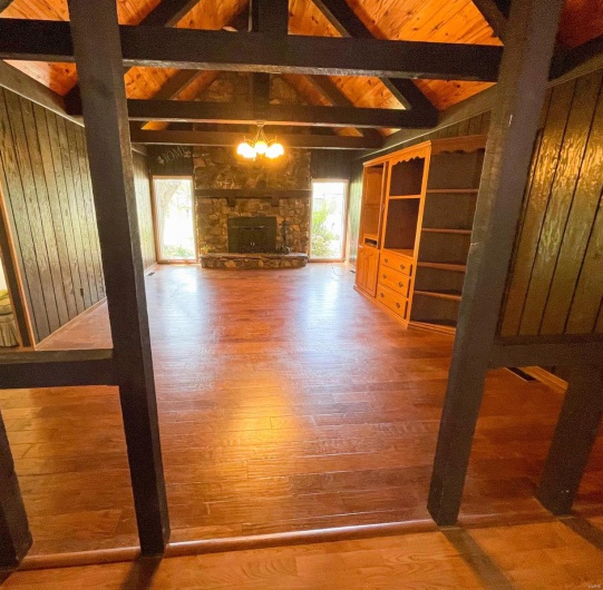 Unfurnished living room with a chandelier, wood finished floors, lofted ceiling with beams, and wooden ceiling
