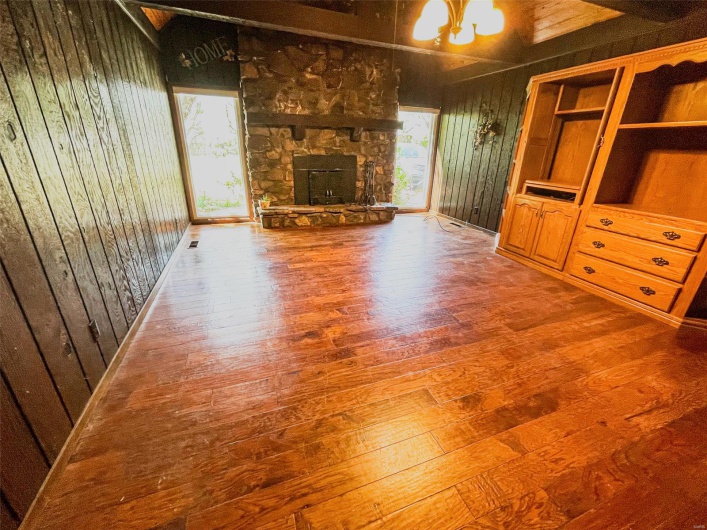 Unfurnished living room featuring a stone fireplace, an inviting chandelier, vaulted ceiling, wood walls, and hardwood / wood-style floors