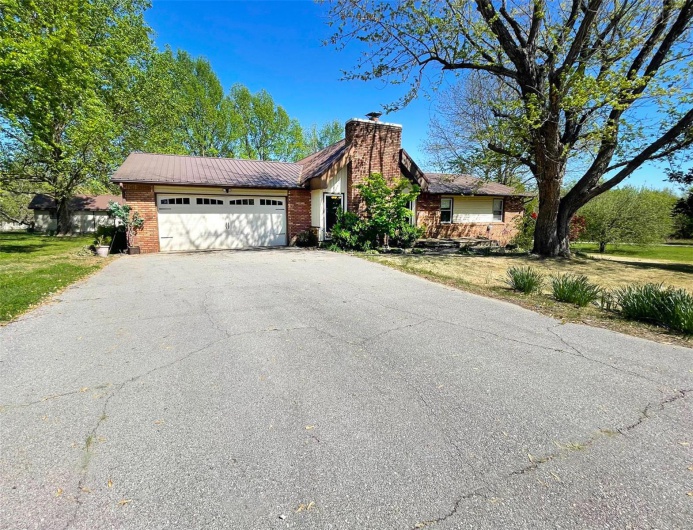 Ranch-style home with an attached garage, a chimney, aphalt driveway, brick siding, and a front lawn