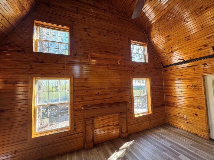 Unfurnished living room featuring wood ceiling, wood finished floors, high vaulted ceiling, and wooden walls