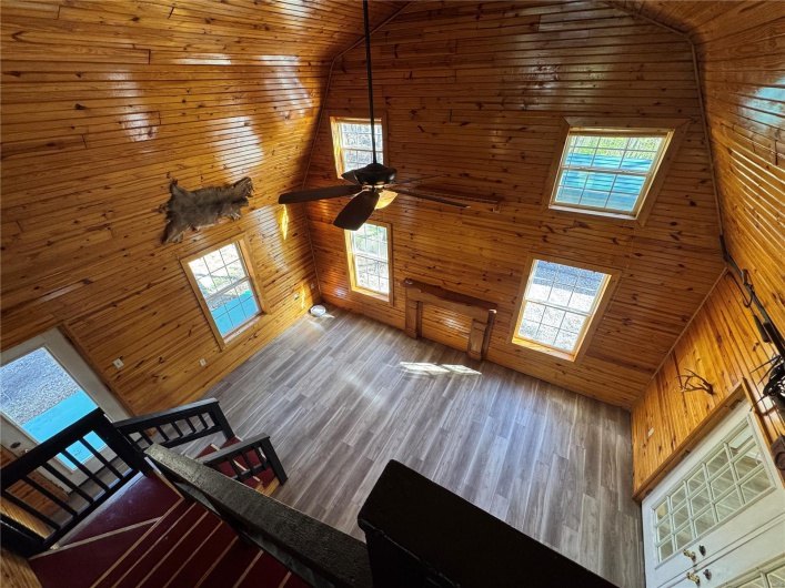 Unfurnished living room featuring high vaulted ceiling, wood walls, wooden ceiling, and a healthy amount of sunlight