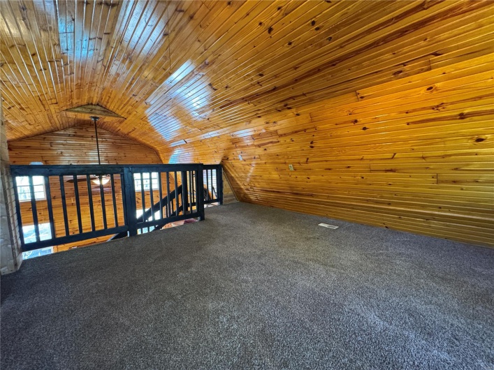 Additional living space with wood walls, carpet, and lofted ceiling