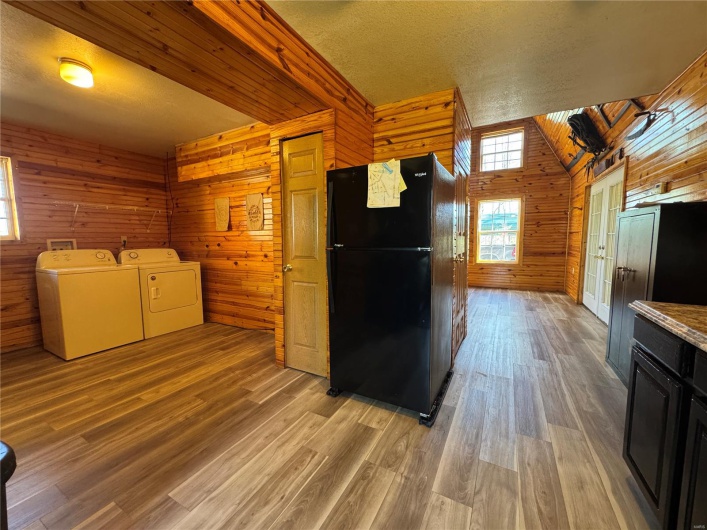 Kitchen featuring freestanding refrigerator, dark cabinetry, wooden walls, light wood finished floors, and washing machine and clothes dryer