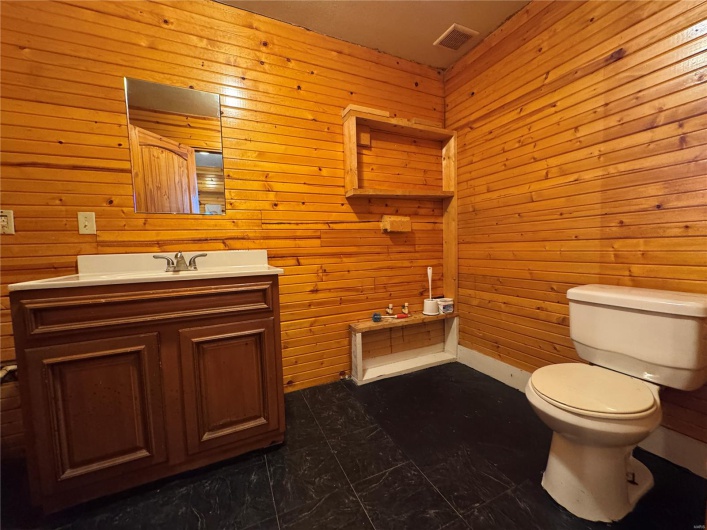 Half bathroom with wood walls, vanity, visible vents, and toilet