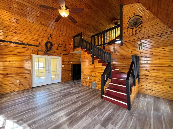 Stairs featuring wood walls, a ceiling fan, wood finished floors, french doors, and high vaulted ceiling