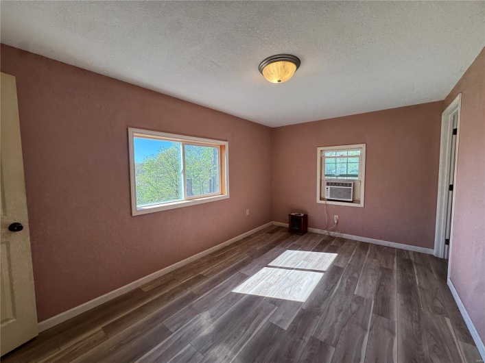 Empty room with baseboards, cooling unit, wood finished floors, and a textured ceiling