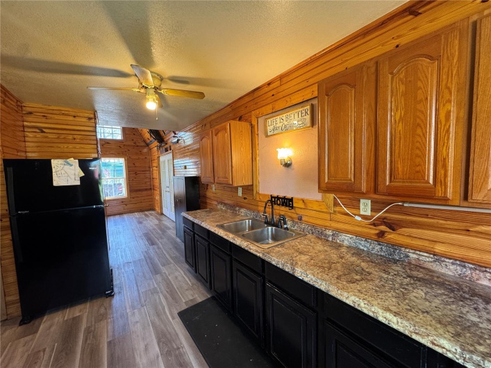 Kitchen with light wood-style flooring, freestanding refrigerator, a ceiling fan, wood walls, and a sink