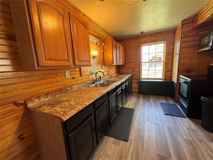 Kitchen with a sink, light wood-type flooring, a textured ceiling, brown cabinetry, and black range with electric stovetop