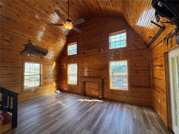 Unfurnished living room with high vaulted ceiling, a ceiling fan, wooden ceiling, wood walls, and wood finished floors