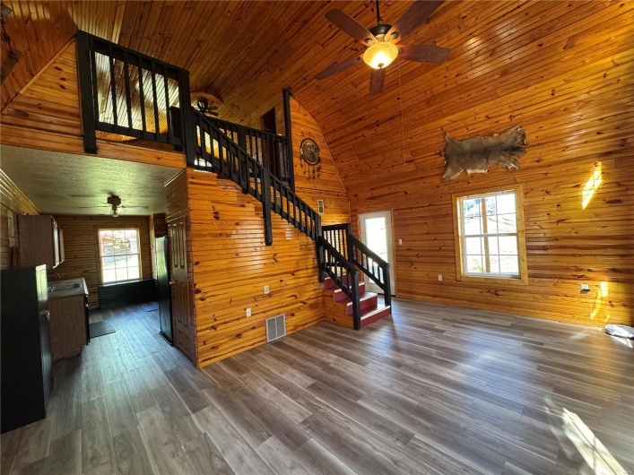 Unfurnished living room with wooden walls, visible vents, a ceiling fan, and stairs