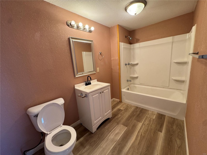 Bathroom with vanity, shower / tub combination, a textured ceiling, toilet, and wood finished floors