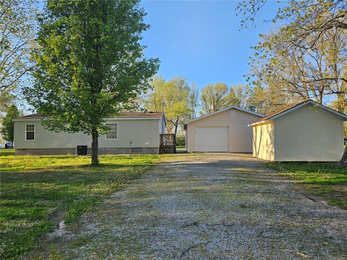 View of property exterior featuring a detached garage, driveway, crawl space, an outbuilding, and a lawn