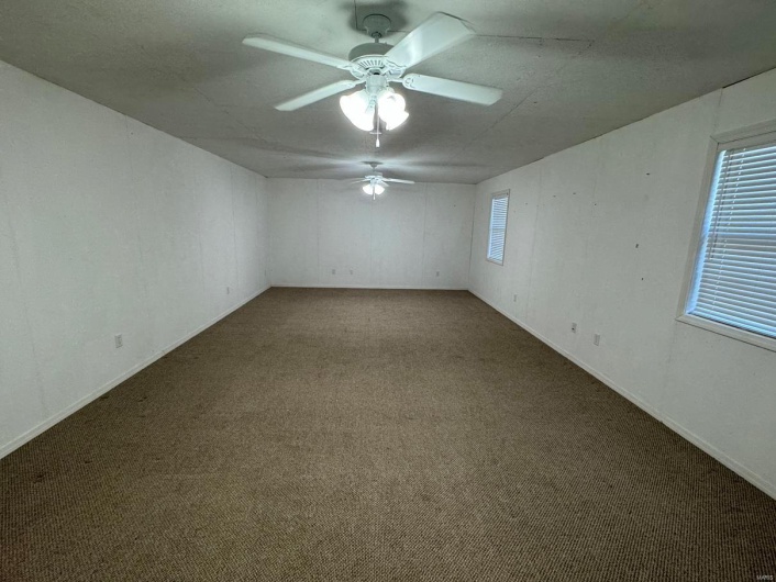 Spare room with ceiling fan and dark colored carpet