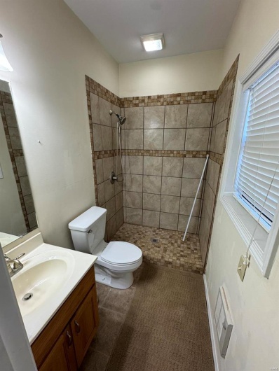 Bathroom featuring visible vents, toilet, a tile shower, a healthy amount of sunlight, and vanity