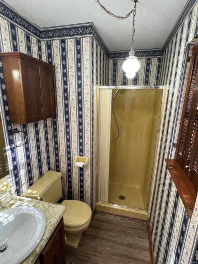 Bathroom with toilet, a textured ceiling, a shower stall, wood finished floors, and wallpapered walls