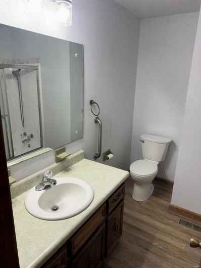 Bathroom with visible vents, toilet, vanity, wood finished floors, and a shower with door