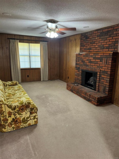 Living room featuring wood walls, a textured ceiling, carpet flooring, and a fireplace