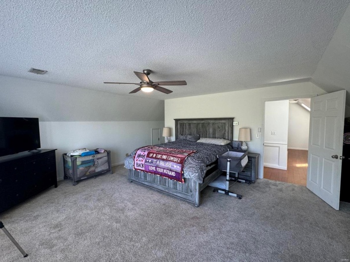 Carpeted bedroom featuring a textured ceiling, ceiling fan, lofted ceiling, and visible vents