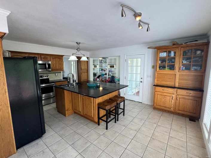 Kitchen featuring dark countertops, a kitchen island with sink, crown molding, stainless steel appliances, and light tile patterned flooring