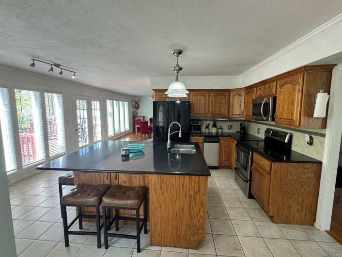 Kitchen with a sink, appliances with stainless steel finishes, a kitchen breakfast bar, dark countertops, and a textured ceiling