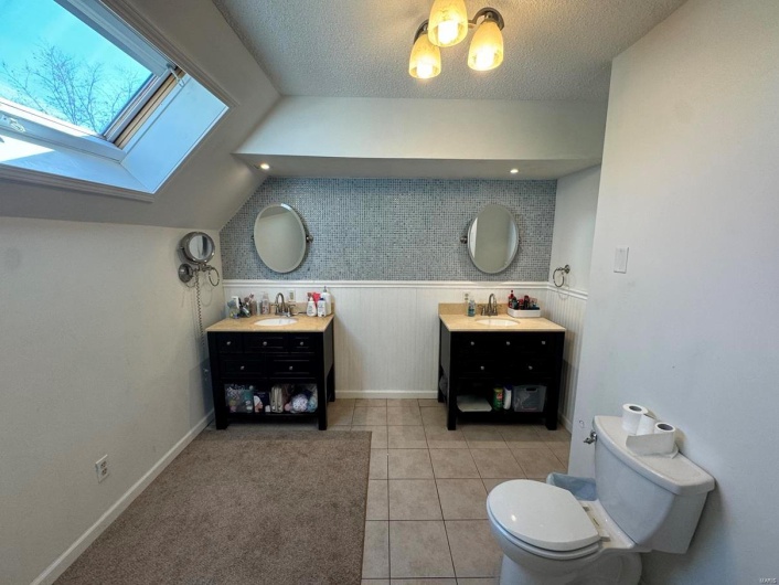 Bathroom featuring tile patterned floors, toilet, vanity, and lofted ceiling with skylight