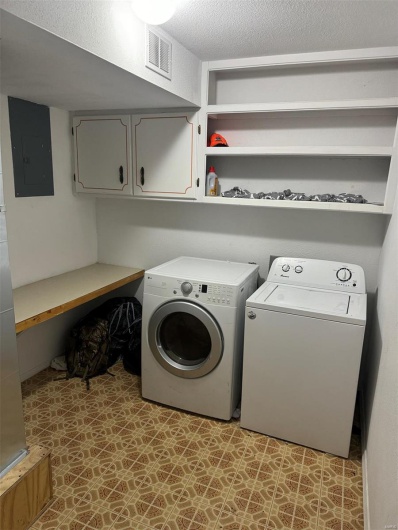 Laundry area featuring light floors, visible vents, electric panel, washing machine and clothes dryer, and cabinet space