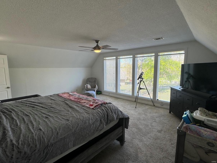 Bedroom with visible vents, ceiling fan, a textured ceiling, light colored carpet, and lofted ceiling