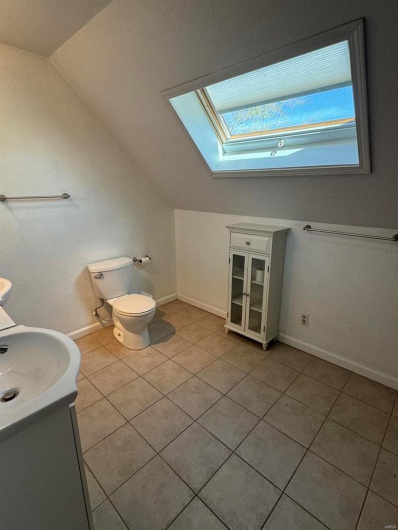 Half bathroom with vaulted ceiling with skylight, vanity, tile patterned flooring, toilet, and baseboards