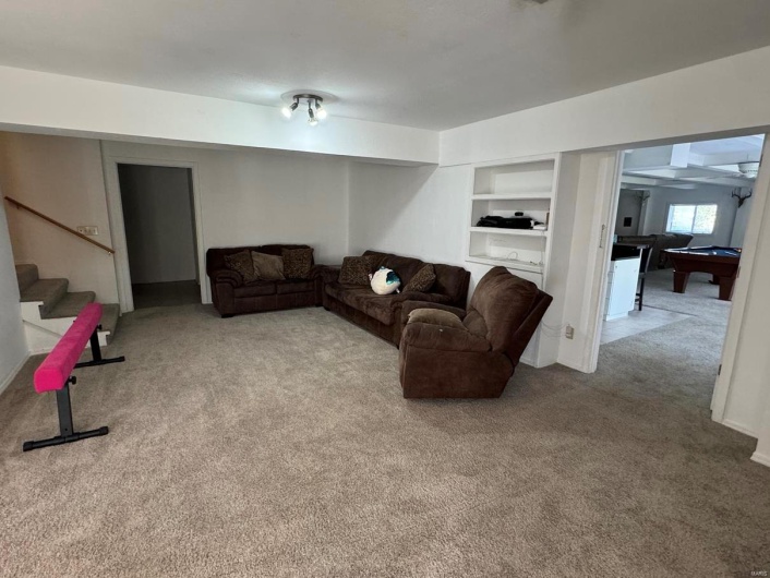 Carpeted living area featuring stairs, built in shelves, and billiards
