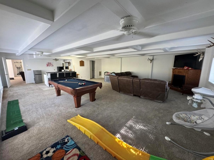 Playroom featuring carpet floors, beam ceiling, pool table, and a fireplace with raised hearth