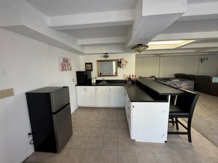 Kitchen with a peninsula, open floor plan, freestanding refrigerator, light tile patterned flooring, and dark countertops