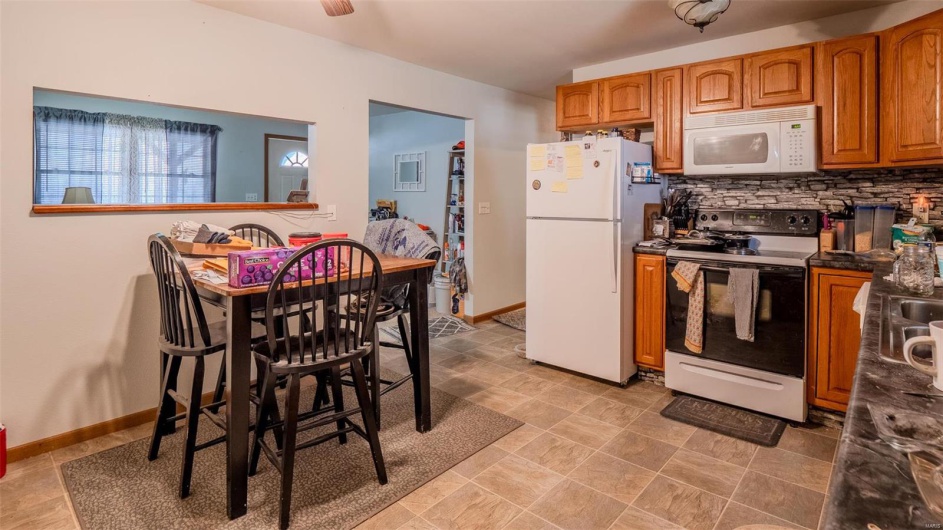 Kitchen featuring brown cabinetry, decorative backsplash, white appliances, and baseboards