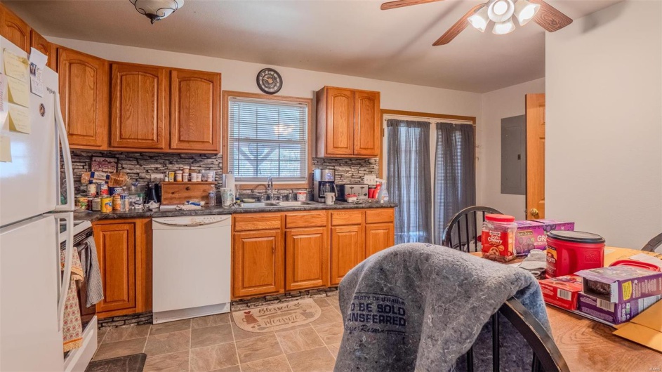 Kitchen with brown cabinets, a sink, dark countertops, tasteful backsplash, and white appliances