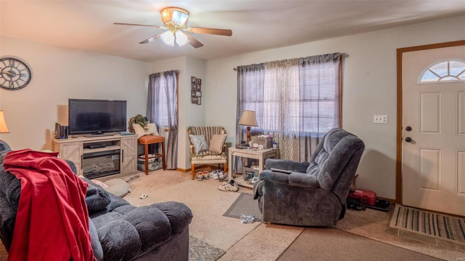 Carpeted living area with a ceiling fan and baseboards