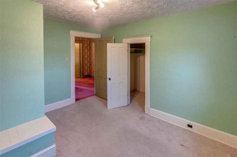 Unfurnished bedroom with a closet, a textured ceiling, baseboards, light carpet, and a textured wall