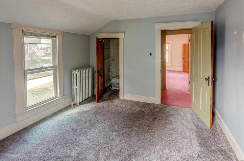 Unfurnished bedroom with lofted ceiling, baseboards, a textured ceiling, carpet floors, and radiator heating unit