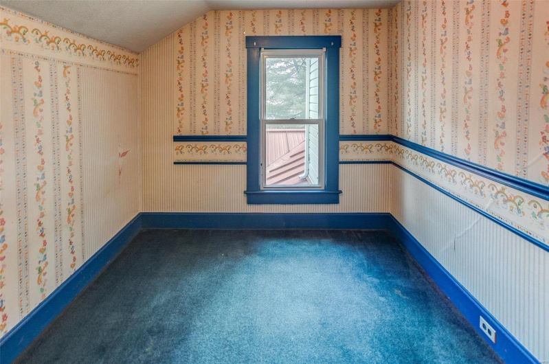 Spare room featuring wallpapered walls, carpet, baseboards, and vaulted ceiling