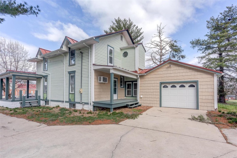 View of front of home featuring a wall mounted AC, covered porch, a garage, and concrete driveway