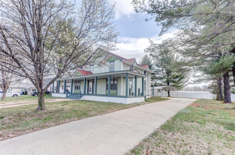Victorian-style house with a detached carport, a front yard, covered porch, and driveway