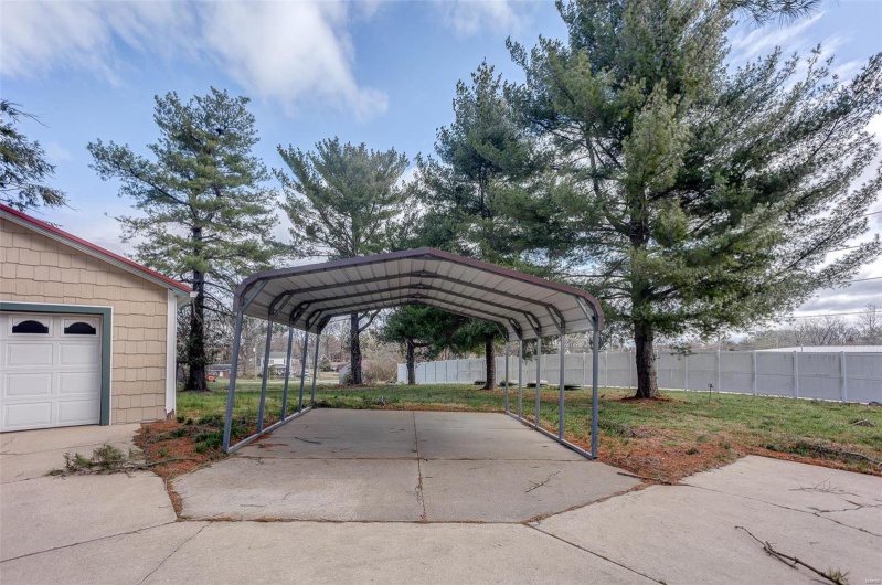 View of car parking featuring fence, concrete driveway, and a carport