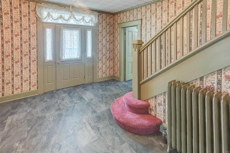 Entryway featuring radiator heating unit, wallpapered walls, baseboards, and stairway