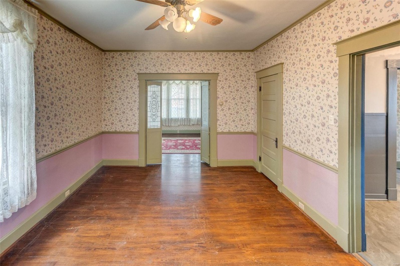 Unfurnished room featuring a wainscoted wall, crown molding, wallpapered walls, wood finished floors, and a ceiling fan
