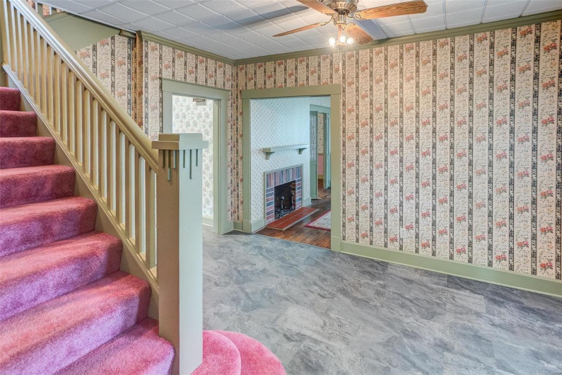 Stairway with crown molding, baseboards, wallpapered walls, a ceiling fan, and a fireplace