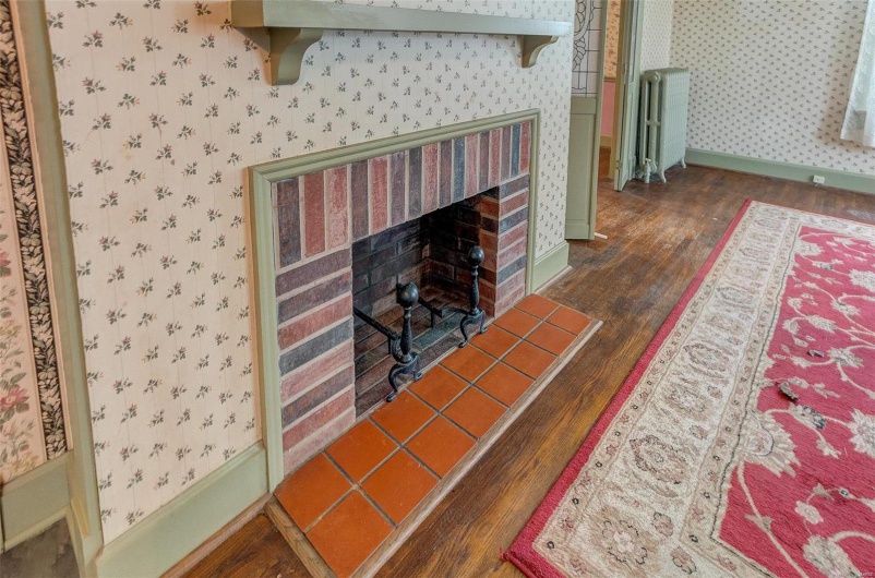 Living room featuring baseboards, wallpapered walls, radiator heating unit, a brick fireplace, and wood finished floors