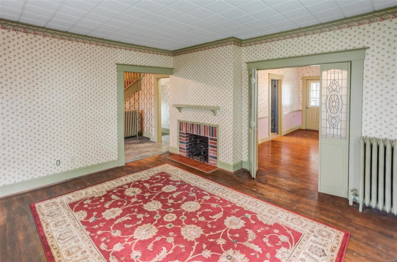 Living room with radiator heating unit, wallpapered walls, baseboards, and wood finished floors