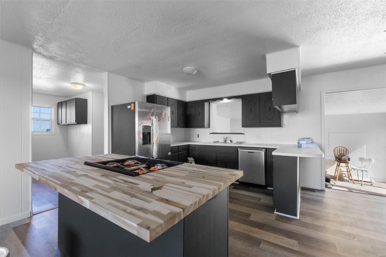 Kitchen with a textured ceiling, a sink, wooden counters, appliances with stainless steel finishes, and dark wood-type flooring