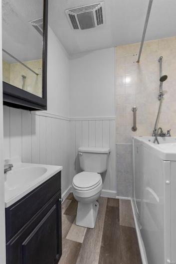 Bathroom with a wainscoted wall, toilet, visible vents, wood finished floors, and vanity